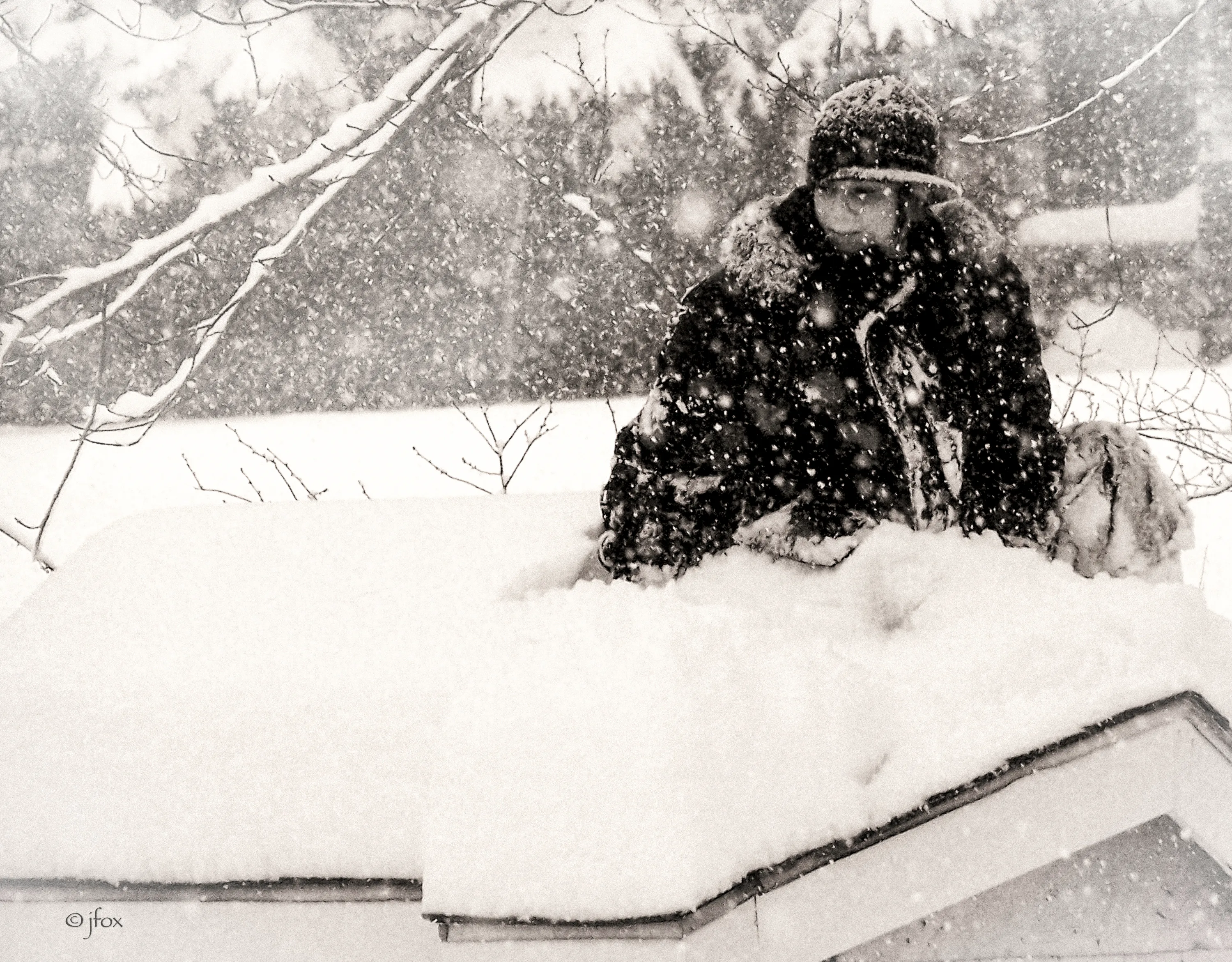 Young child sitting on a rooftop while snow is falling.